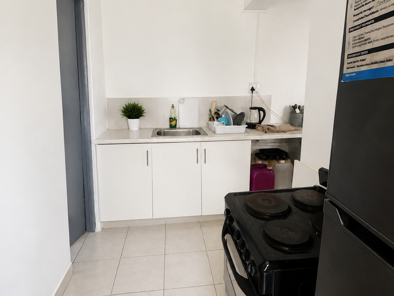 A compact kitchen area featuring white cabinetry, a stainless steel sink, tiled splashback, and ceramic floor tiles.