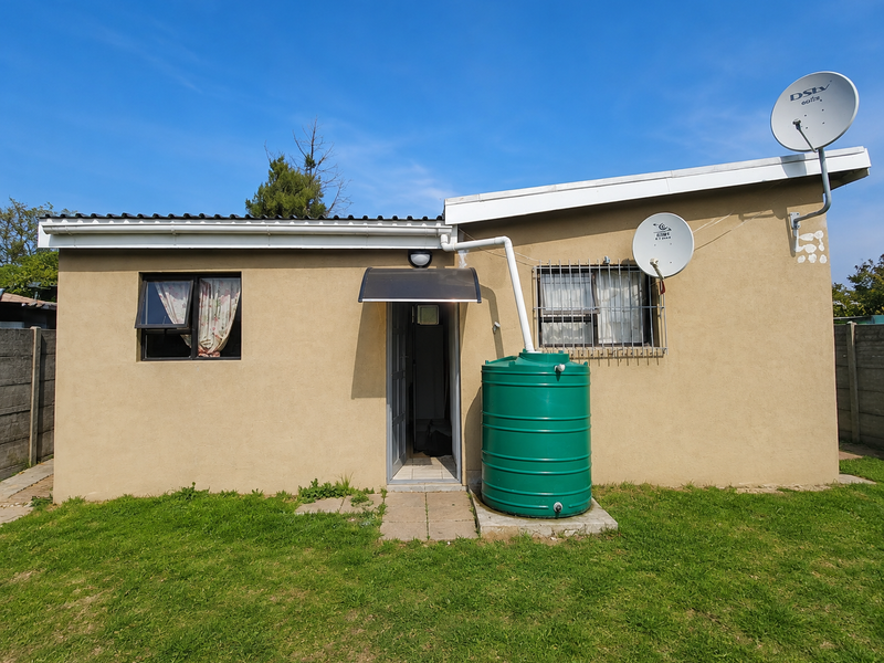 Rear exterior view of the apartment featuring a water tank, satellite dish, security bars on windows, and a small entrance awning.