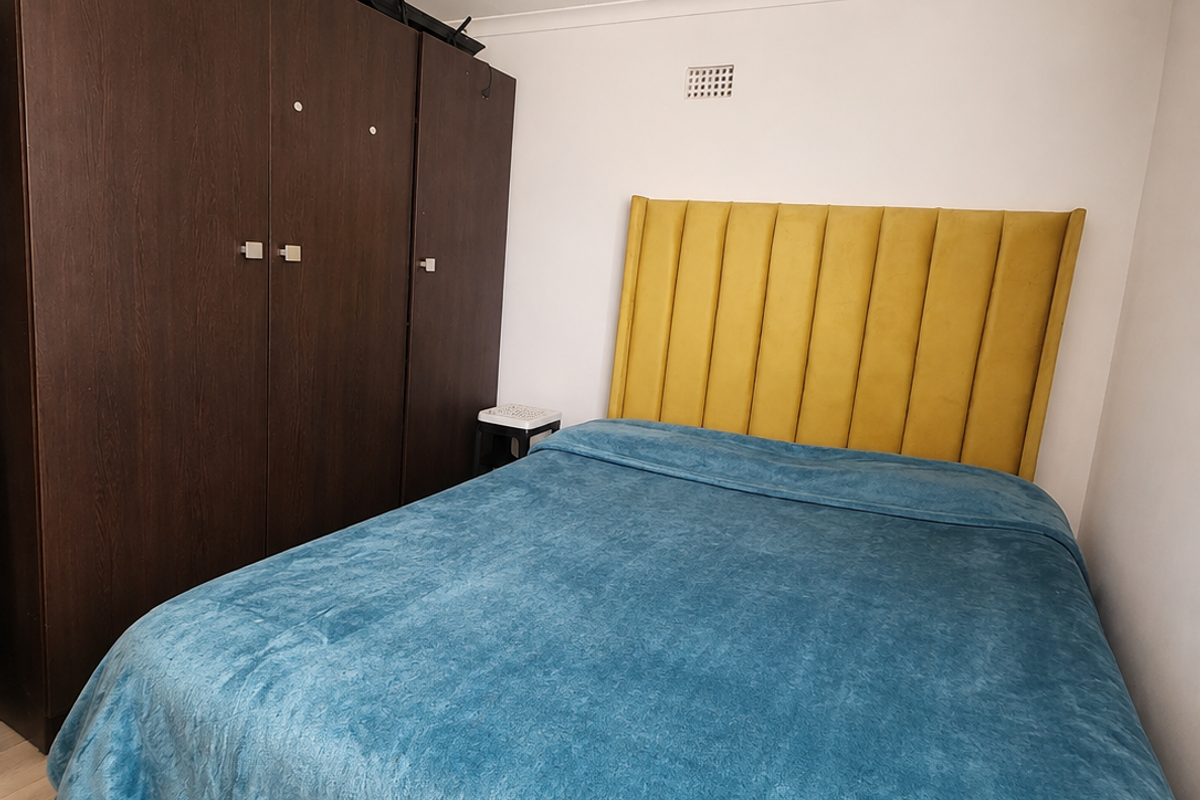 A bedroom featuring a dark wood built-in wardrobe and a yellow upholstered headboard, finished with light-toned flooring and coving.