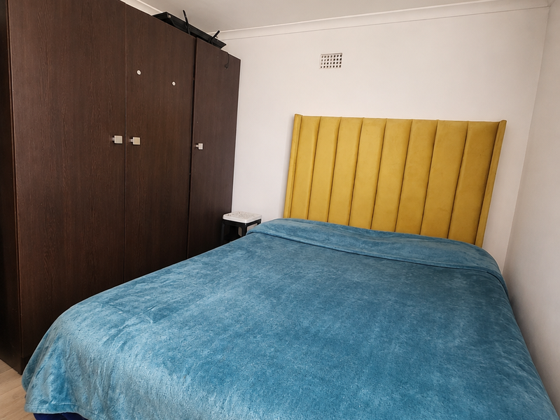 A bedroom featuring a dark wood built-in wardrobe and a yellow upholstered headboard, finished with light-toned flooring and coving.