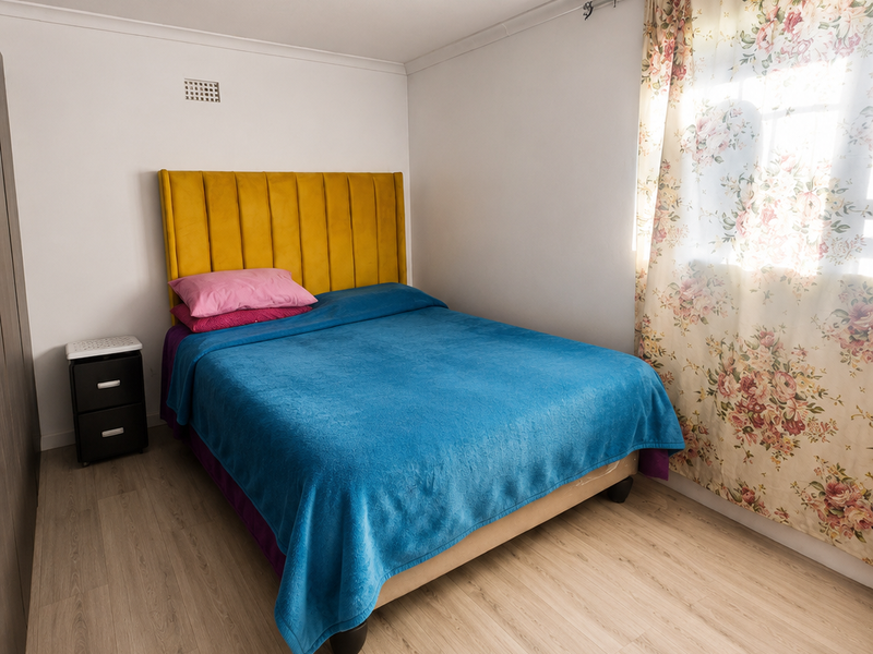 A well-maintained bedroom featuring light-toned laminate flooring, neutral walls, and a functional ventilation grille.