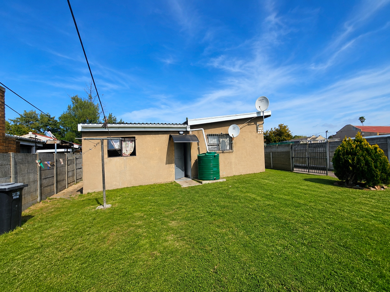 Rear view of the property featuring a lawn, water tank, satellite dish, and perimeter security fencing.