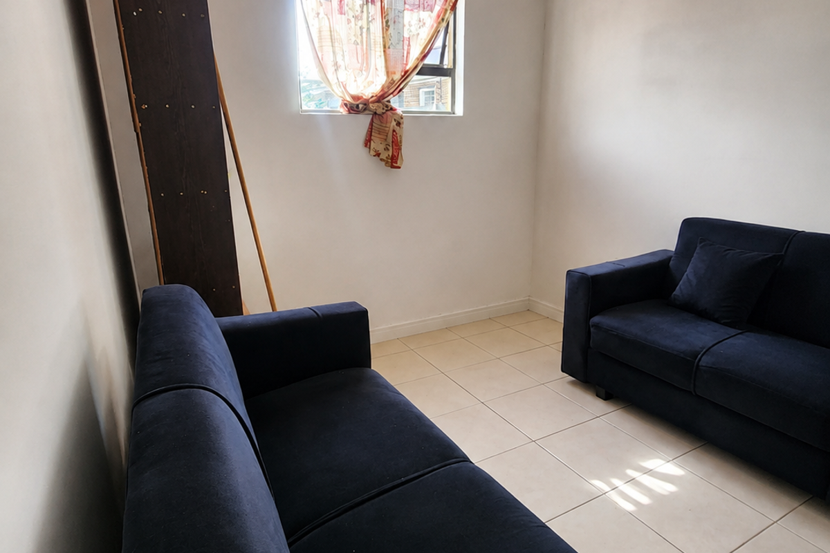A living room area featuring neutral tiled flooring and a single window, providing a simple and functional space for relaxation.