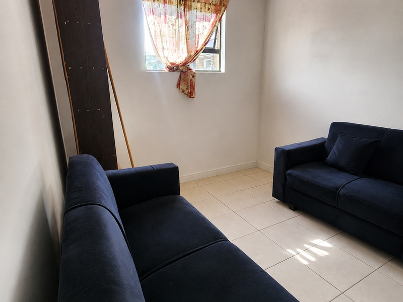 A living room area featuring neutral tiled flooring and a single window, providing a simple and functional space for relaxation.