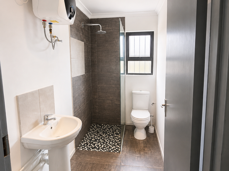 A modern bathroom featuring a pedestal basin, a walk-in shower with a rain shower head, and a toilet, finished with contemporary floor and wall tiles.
