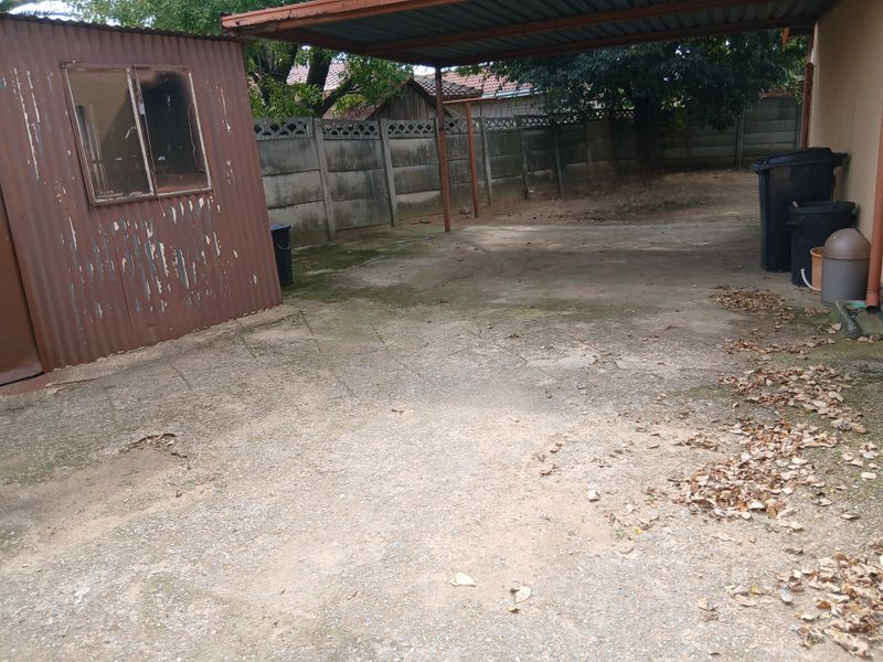 Rear exterior area featuring a corrugated metal shed, a covered carport, and concrete paving enclosed by a precast boundary wall.
