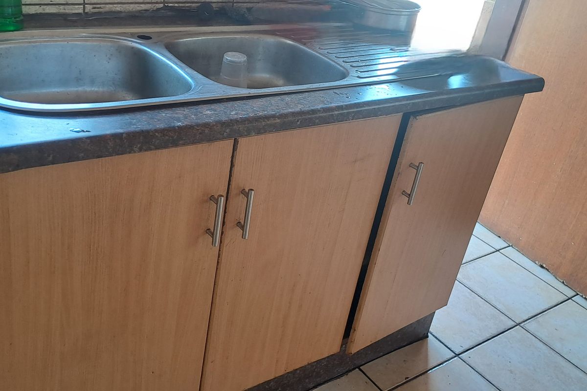 A compact kitchen area featuring a double bowl stainless steel sink, laminate countertop, and built-in base cabinetry with ceramic tiled flooring.