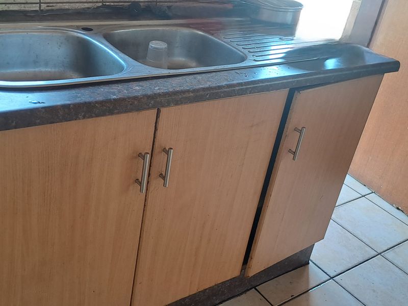 A compact kitchen area featuring a double bowl stainless steel sink, laminate countertop, and built-in base cabinetry with ceramic tiled flooring.