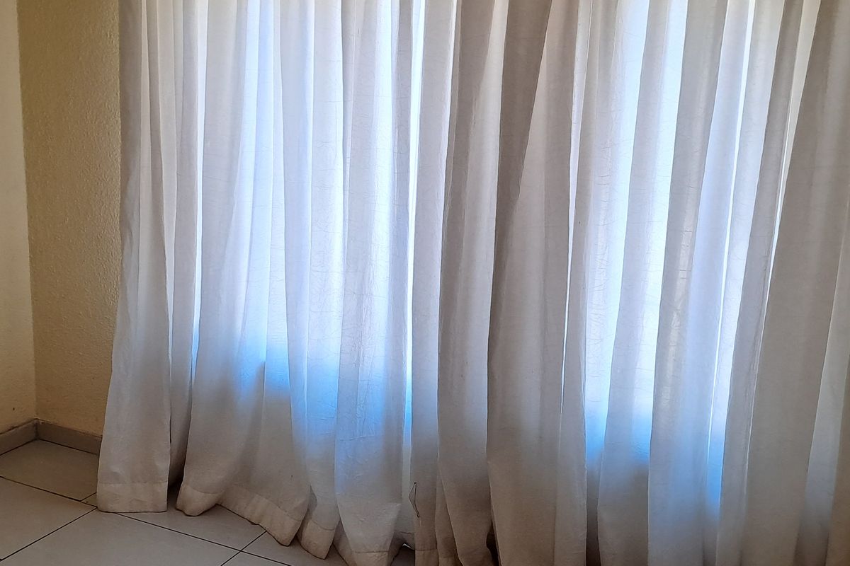 An empty room featuring tiled flooring and wall-mounted curtain tracks, requiring cosmetic updates to the wall finishes.