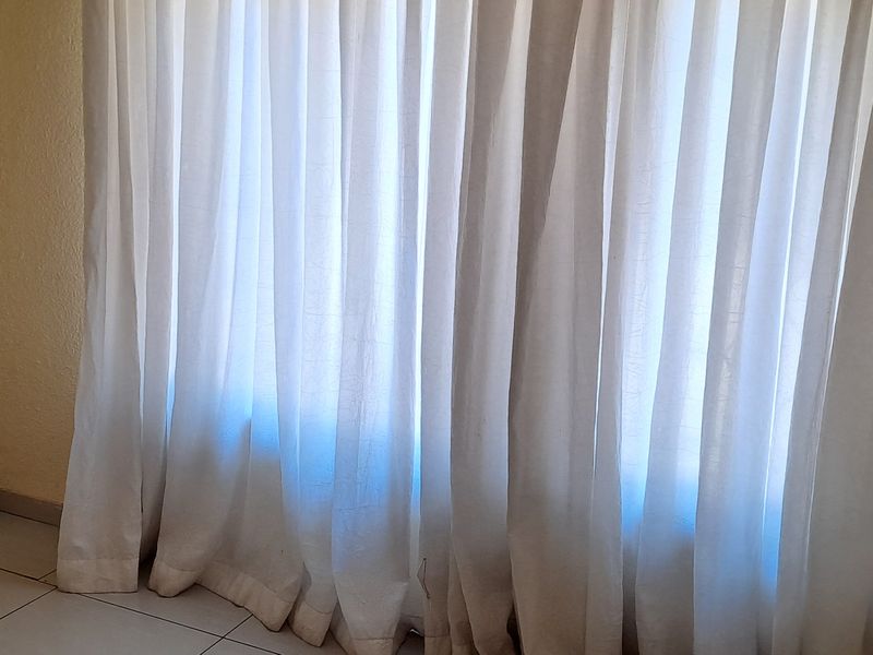An empty room featuring tiled flooring and wall-mounted curtain tracks, requiring cosmetic updates to the wall finishes.