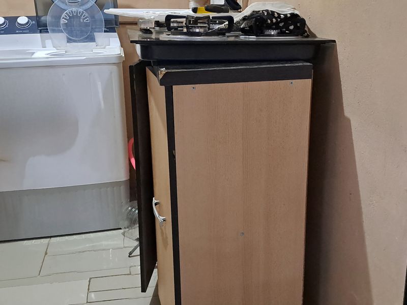 A compact laundry area featuring tiled flooring and a small cabinet unit with a built-in gas hob.