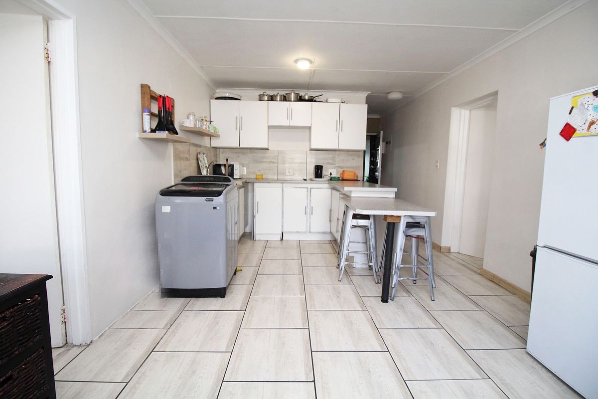 A functional kitchen featuring white cabinetry, tiled backsplash, and a breakfast bar, with tiled flooring throughout the space.