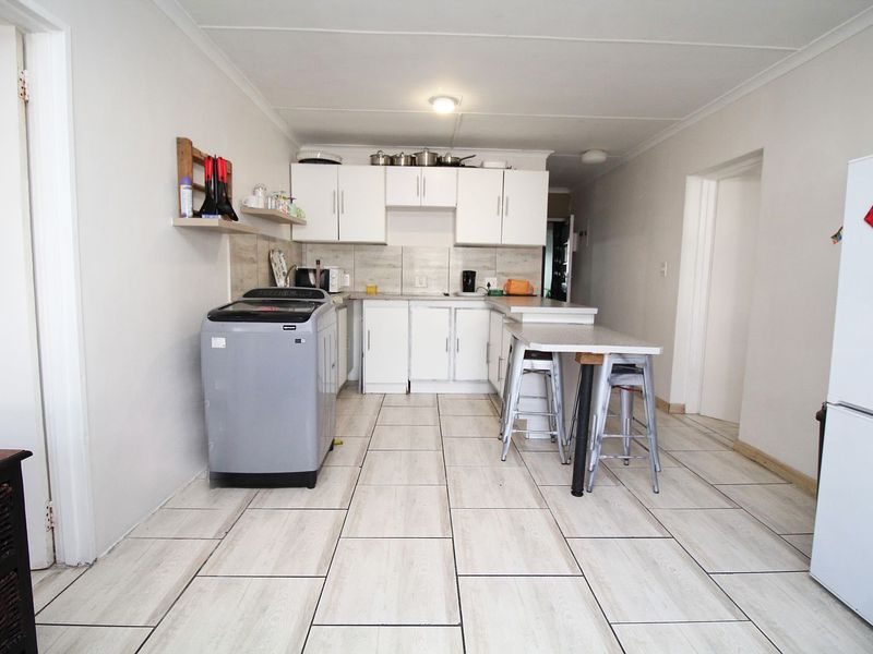 A functional kitchen featuring white cabinetry, tiled backsplash, and a breakfast bar, with tiled flooring throughout the space.