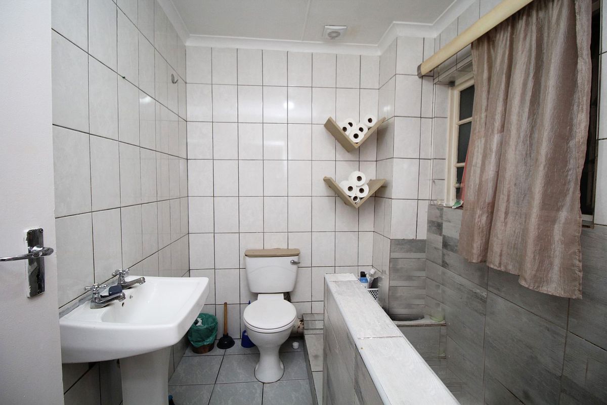 A functional bathroom featuring a pedestal washbasin, toilet, and tiled finishes. The space would benefit from cosmetic updates to modernize the fixtures and tiling.