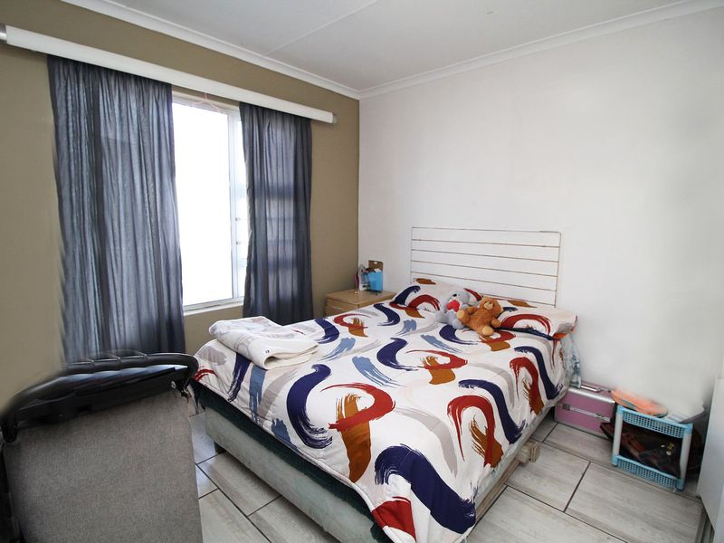 A standard bedroom featuring tiled flooring and a window with an installed curtain rail.