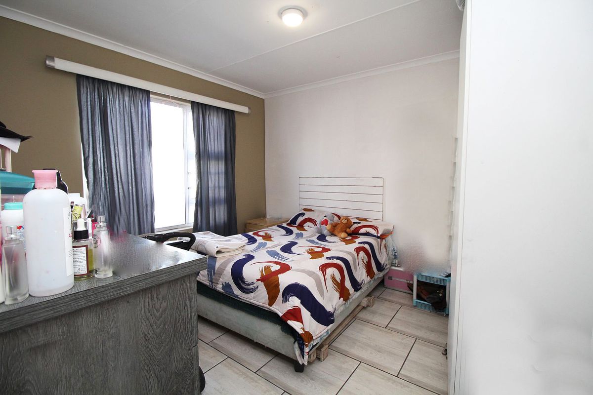 A functional bedroom featuring tiled flooring, a built-in cupboard, and a window with curtain rails, providing a practical living space.