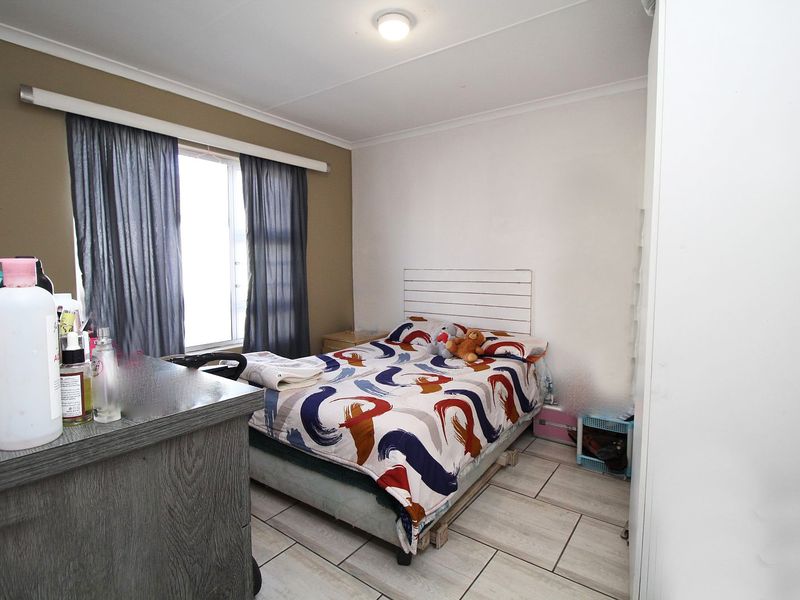 A functional bedroom featuring tiled flooring, a built-in cupboard, and a window with curtain rails, providing a practical living space.