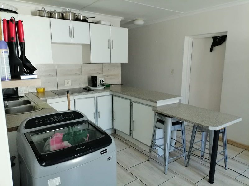 Functional kitchen featuring white cabinetry, laminate countertops, tiled backsplash, and integrated hob, offering a practical layout for daily meal preparation.
