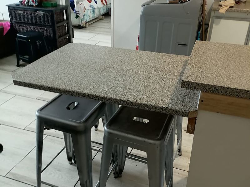 A kitchen area featuring a breakfast bar with laminate countertops and tiled flooring, showing signs of wear and unfinished cabinetry edges.