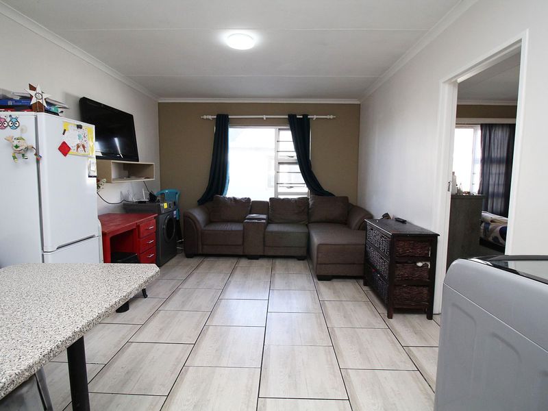 An open-plan living area featuring light-toned tiled flooring and a louvered window, providing a functional space for daily living.