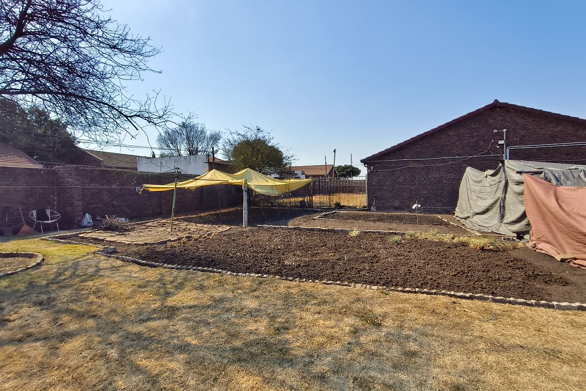 A spacious rear garden area featuring brick boundary walls, raised garden beds with brick edging, and a rotary clothesline.
