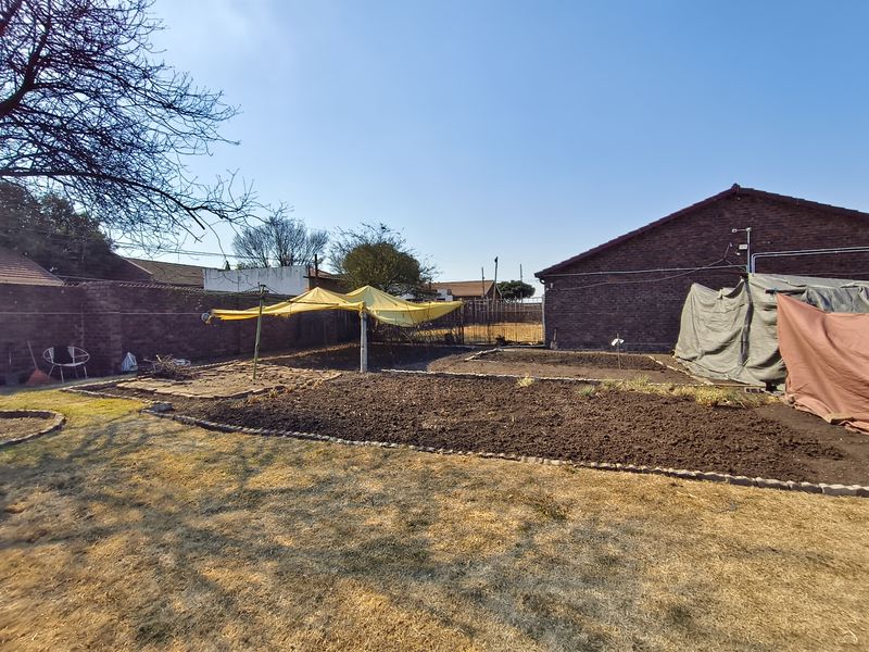 A spacious rear garden area featuring brick boundary walls, raised garden beds with brick edging, and a rotary clothesline.