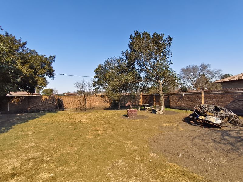A spacious residential garden featuring a brick perimeter wall, mature trees, and a decorative brick wishing well structure.