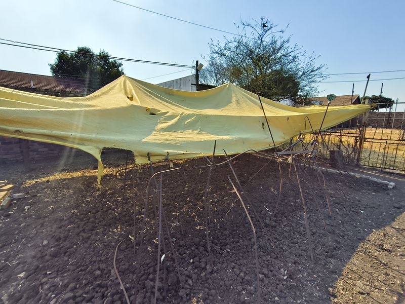 A vacant residential plot featuring exposed soil, perimeter fencing, and a temporary makeshift shade structure.