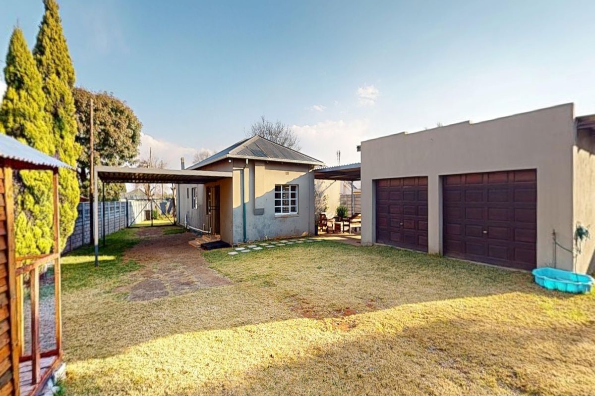Rear view of the property featuring a double garage, attached carport, and a spacious backyard area with boundary walling.