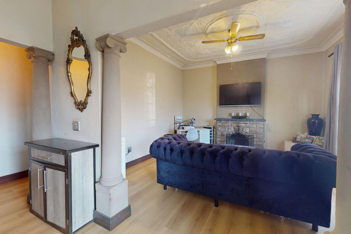 A living room featuring a stone fireplace, decorative ceiling molding with a ceiling fan, and classical columns separating the space.