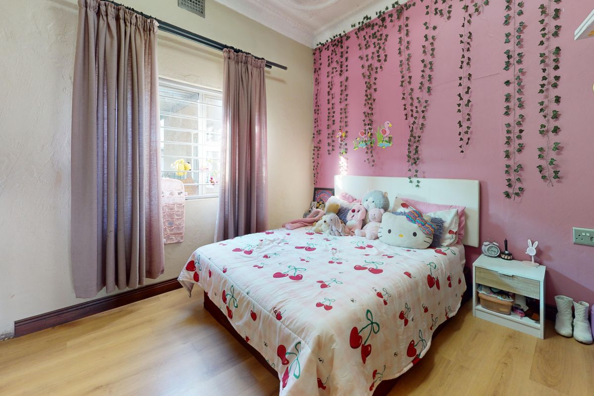 A bedroom featuring laminate flooring, decorative ceiling cornice, and a window with security bars. The walls show signs of wear and uneven plaster.