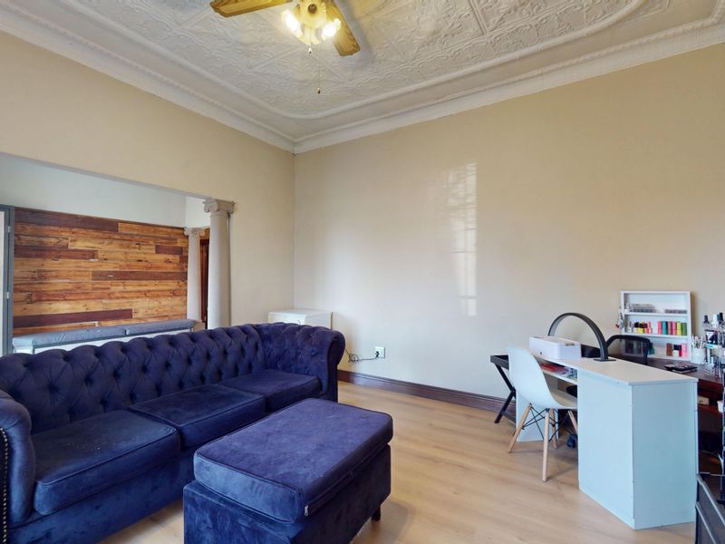 Spacious living area featuring a unique pressed metal ceiling, decorative ceiling rose, stone fireplace, and classical columns separating the space.