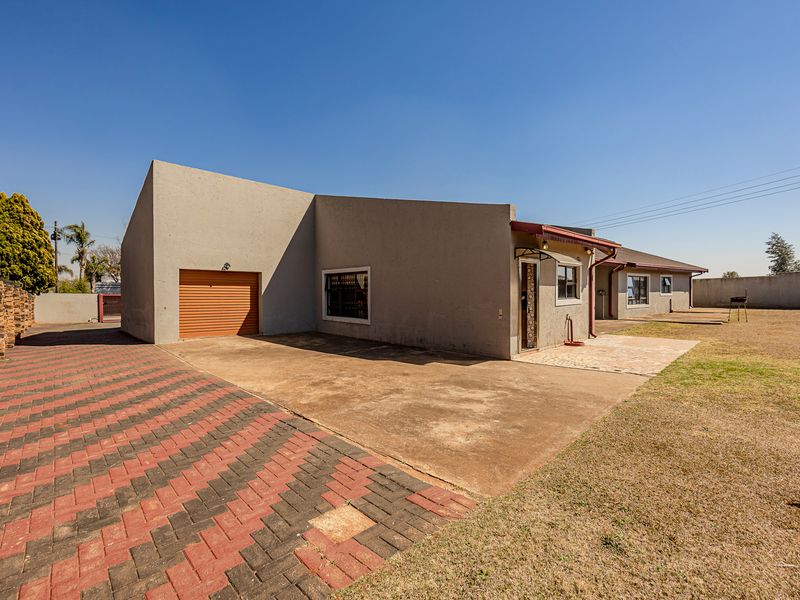 Front exterior view of the property featuring a single garage, paved driveway, and a concrete entrance area with surrounding boundary walls.