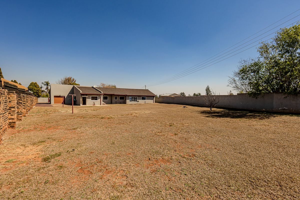 Spacious rear yard featuring a large lawn area, perimeter walling, and a view of the rear building elevation with garage access.