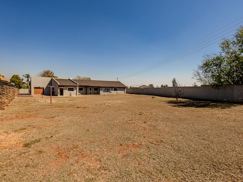 Spacious rear yard featuring a large lawn area, perimeter walling, and a view of the rear building elevation with garage access.
