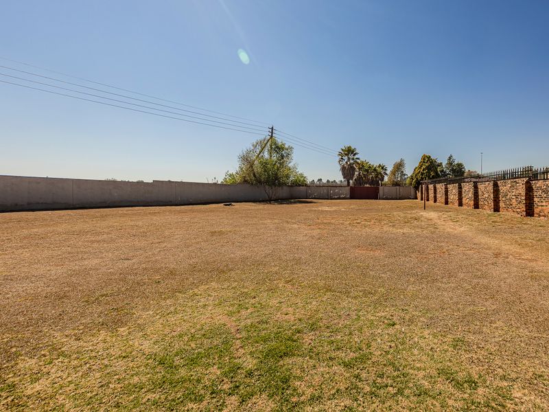 A large, open, and level backyard area enclosed by a combination of concrete and brick perimeter walls with security fencing.