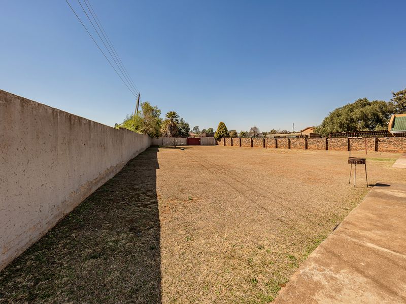 A spacious, open rear yard featuring a large lawn area, concrete paving, and secure perimeter brick boundary walls.