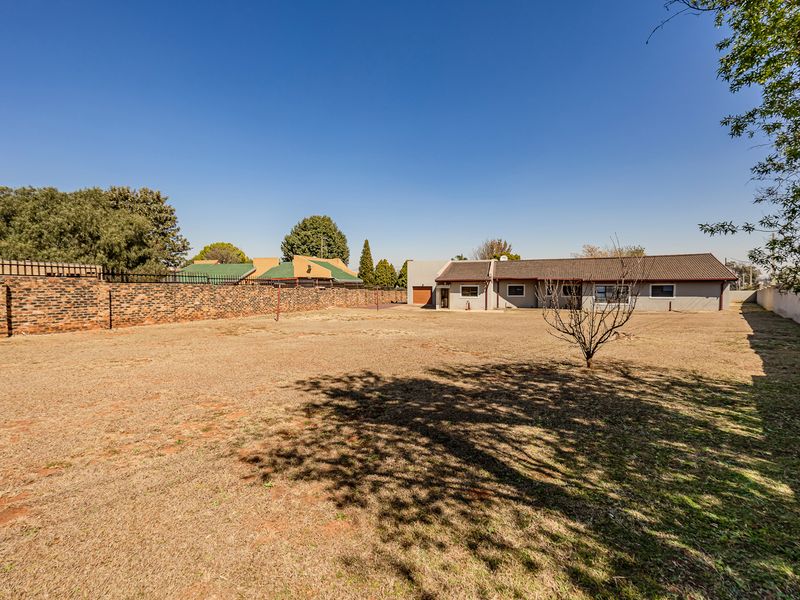 A spacious rear garden featuring a large lawn area, brick boundary walls, and a view of the rear building elevation with a garage.