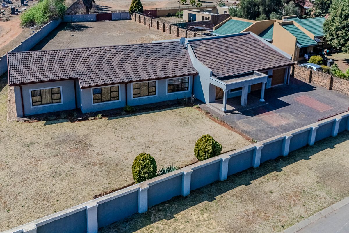 Aerial view of a single-story residential property featuring a tiled roof, paved driveway, attached garage, and a secure perimeter wall.
