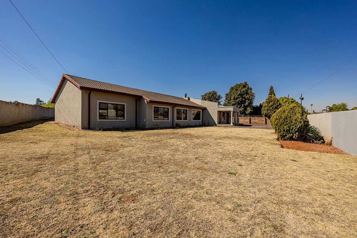 A spacious rear exterior view of the house featuring a large lawn, tiled roof, and perimeter walling.