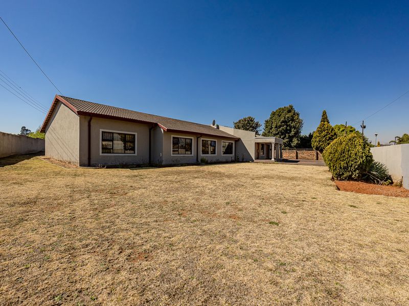 A spacious rear exterior view of the house featuring a large lawn, tiled roof, and perimeter walling.