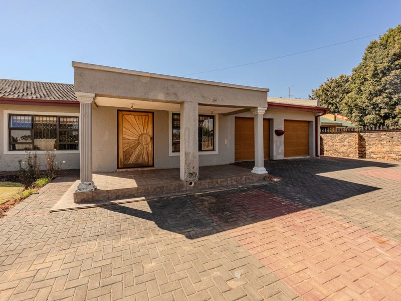 Front elevation of a single-story house featuring a covered entrance porch, decorative columns, a paved driveway, and a double garage.