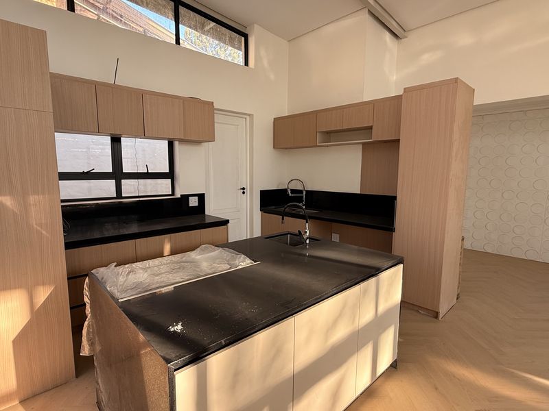 Modern kitchen featuring light wood cabinetry, dark stone countertops, a central island with sink, and high-level clerestory windows providing natural light.