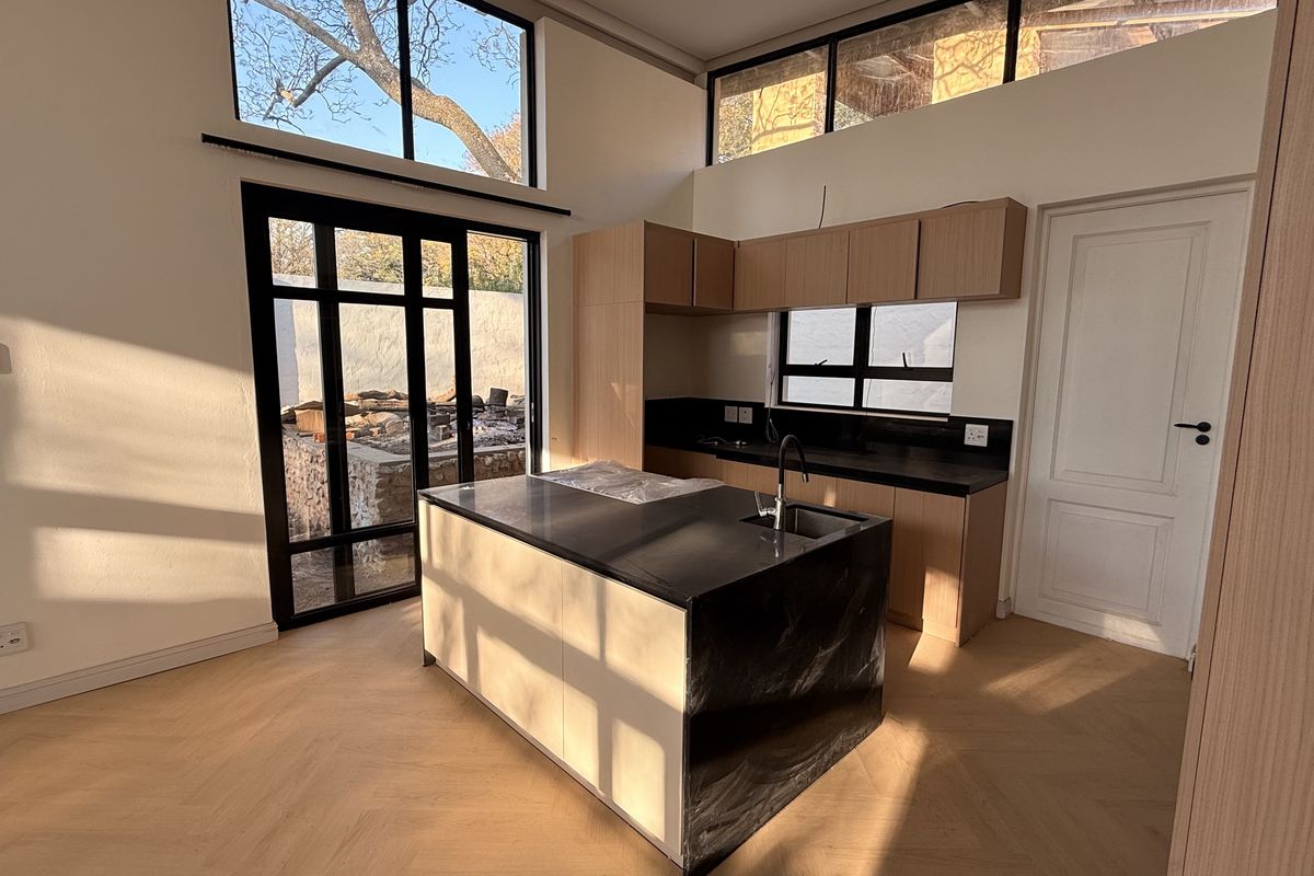 Modern kitchen featuring a central island with stone countertops, light wood cabinetry, herringbone flooring, and large windows providing abundant natural light.
