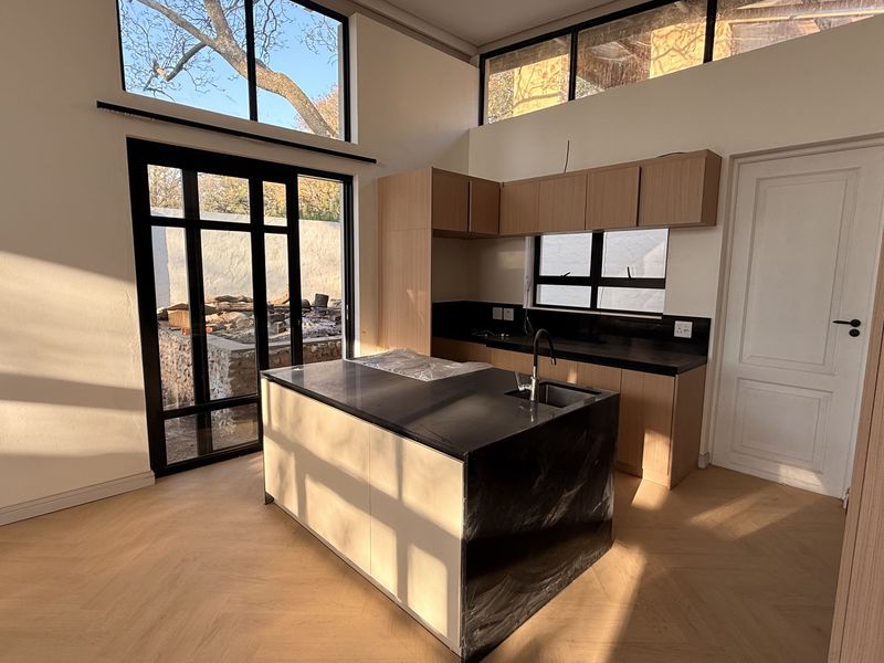 Modern kitchen featuring a central island with stone countertops, light wood cabinetry, herringbone flooring, and large windows providing abundant natural light.