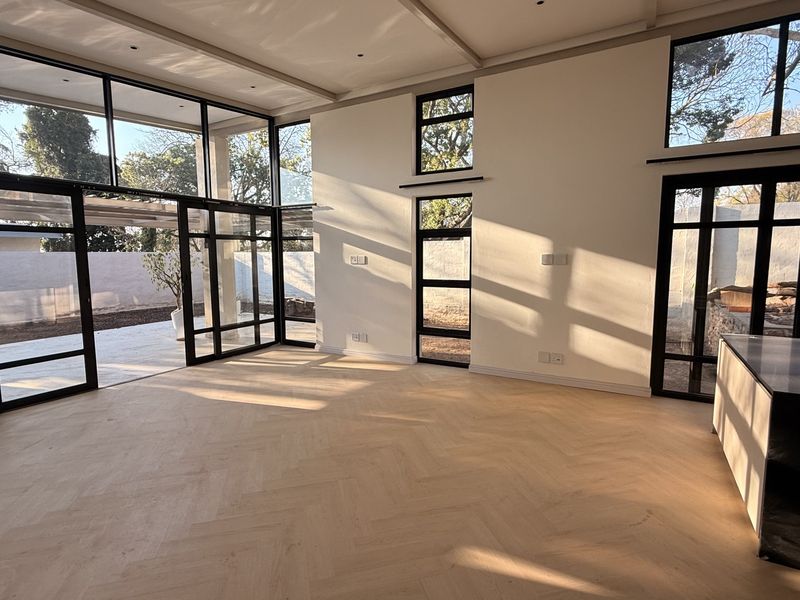 Spacious open-plan living area featuring high ceilings, herringbone timber flooring, and extensive black steel-framed glass doors providing seamless indoor-outdoor flow.