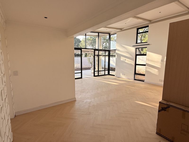 Spacious open-plan living area featuring elegant herringbone timber flooring, modern black-framed glass doors, and a unique textured feature wall with abundant natural light.