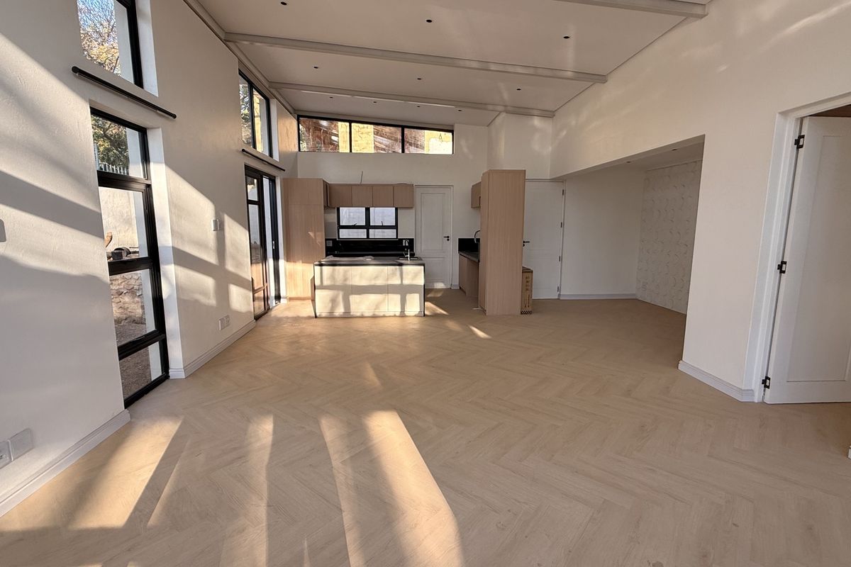 Spacious open-plan living and kitchen area featuring modern herringbone timber flooring, abundant natural light, and contemporary built-in cabinetry.