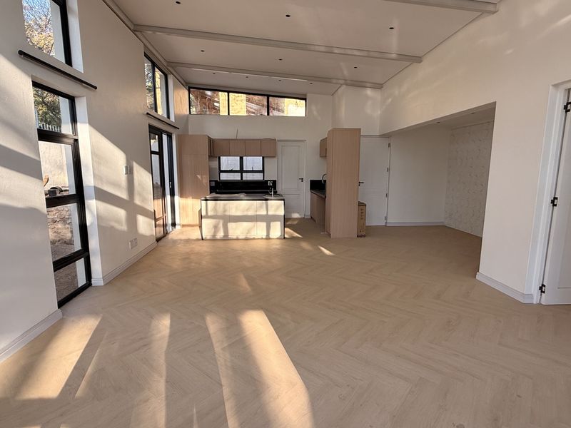 Spacious open-plan living and kitchen area featuring modern herringbone timber flooring, abundant natural light, and contemporary built-in cabinetry.