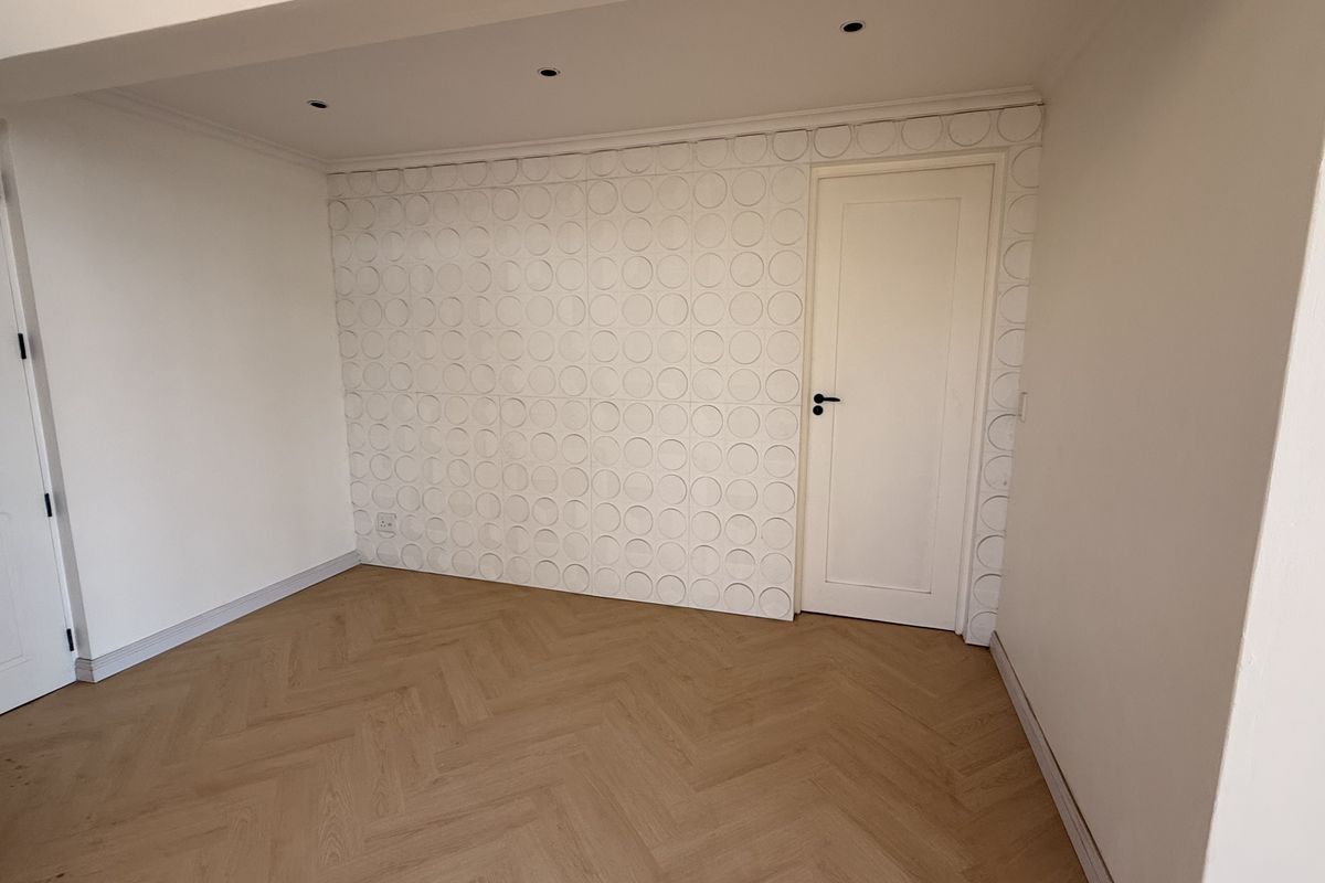 An empty bedroom featuring light wood herringbone flooring, recessed ceiling lighting, and a decorative textured feature wall.